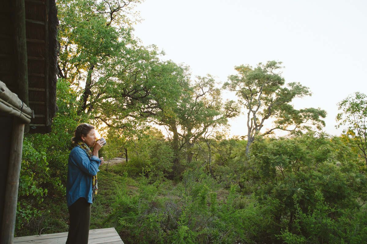 Une femme buvant son thé du matin sur une terrasse en bois face au bush du Kruger à l'aube